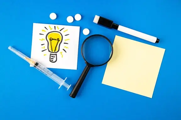 top-view-lightbulb-drawing-with-magnifier-injection-pills-blue-background-hospital-health-covid-lab-science-pandemic-virus-drug-min